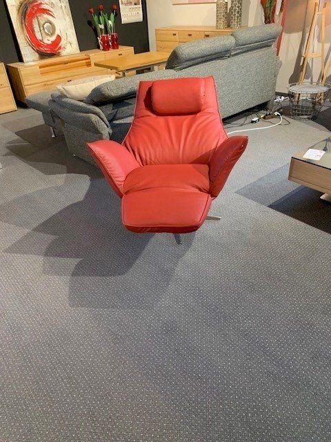 Roter Ledersessel mit Relaxfunktion und ausgefahrener Fußstütze, umgeben von grauen Sofas.