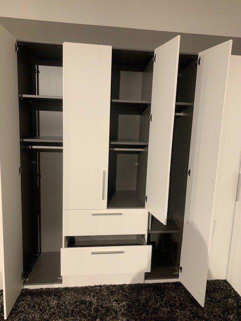 Vollständig geöffneter Eckschrank mit schwarzer Innenausstattung, Schubladen und verschiedenen Fächern für Kleidung.
