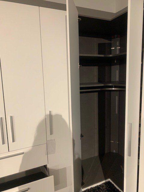 Eckschrank-Innenansicht mit Glasregalbrettern, Kleiderstange und schwarzer Rückwand für maximale Stauraumnutzung.