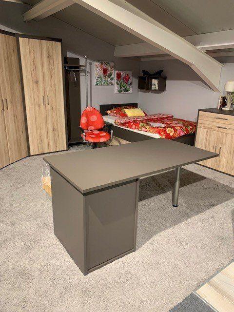 Dachgeschoss-Büro mit anthrazitfarbenem Schreibtisch, Eichenholzmöbeln und rotem Bürostuhl unter Dachschräge.