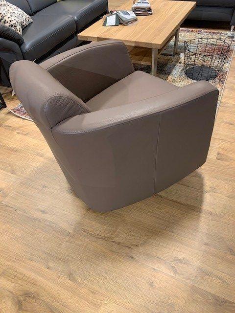 Graubrauner Ledersessel mit abgerundeten Ecken neben Holz-Couchtisch in Wohnambiente.