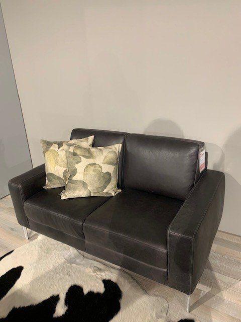 Kompaktes schwarzes Ledersofa mit gemusterten Kissen und Chrombeinen auf schwarz-weißem Kuhfell.