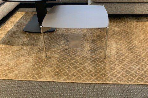 Weißer abgerunder Couchtisch mit matter Oberfläche auf goldfarbenem gemustertem Teppich, Detailaufnahme.