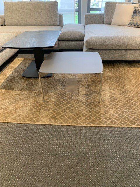 Weißer abgerunder Couchtisch mit matter Oberfläche auf goldfarbenem gemustertem Teppich, Detailaufnahme.