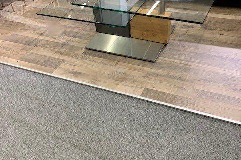 Couchtisch aus Glas mit goldenem Metallgestell vor grauem Sofa in Möbelhaus-Ausstellung.