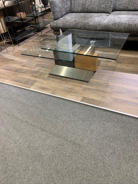 Moderner Glas-Couchtisch mit geometrischem Metallunterbau in Gold- und Silberoptik.