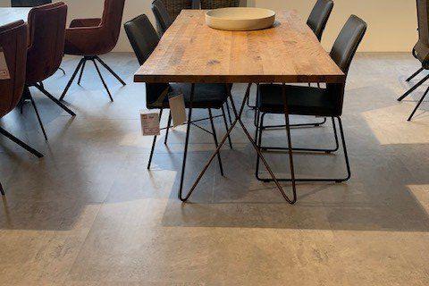Massivholz-Esstisch mit schwarzen Metallstühlen in lichtdurchflutetem Showroom mit Lamellenvorhängen und dekorativen Weidenkörben.