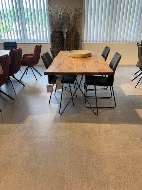 Massivholz-Esstisch mit schwarzen Metallstühlen in lichtdurchflutetem Showroom mit Lamellenvorhängen und dekorativen Weidenkörben.