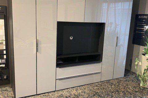 Weiße Medienwand mit integriertem Fernseher und schwarzer Abdeckplatte unter Dachschräge mit weißen Balken.
