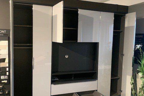 Weiße Medienwand mit integriertem Fernseher und schwarzer Abdeckplatte unter Dachschräge mit weißen Balken.