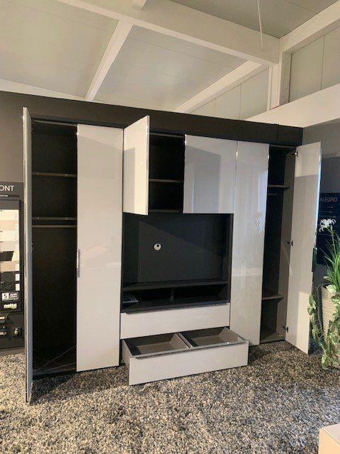 Geöffnete Medienwand zeigt schwarze Innenausstattung mit Regalbrettern und geöffneter Schublade unter dem TV-Fach.