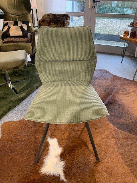 Grüner Cord-Stuhl auf braunem Kuhfell-Teppich in modernem Showroom mit großen Fenstern.