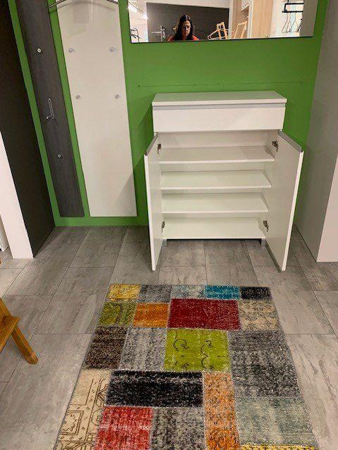 Geöffneter Garderobenschrank zeigt weiße Innenausstattung mit Regalbrettern auf buntem Patchwork-Teppich.