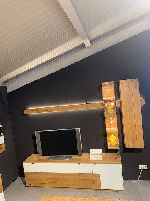 Kompakte Wohnwand-Kombination aus Holz und Weiß mit TV-Bereich und Beleuchtung unter Dachschräge.