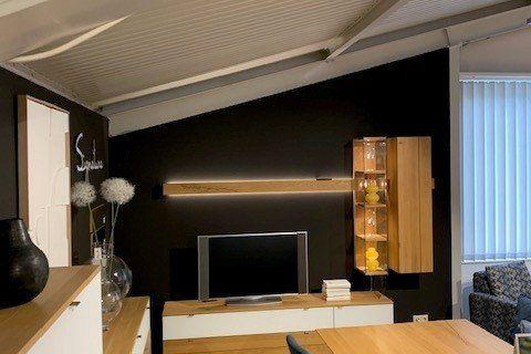 Holz-Wohnwand mit integrierter Beleuchtung und Glasvitrine in modernem Wohnraum mit Holzbalkendecke.