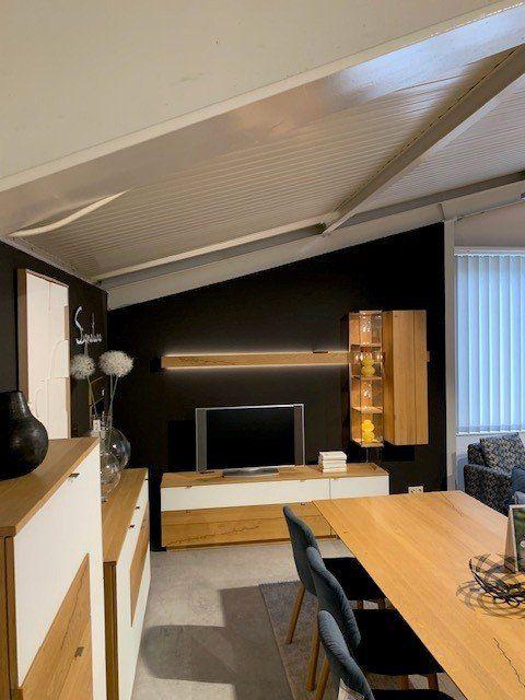 Holz-Wohnwand mit integrierter Beleuchtung und Glasvitrine in modernem Wohnraum mit Holzbalkendecke.