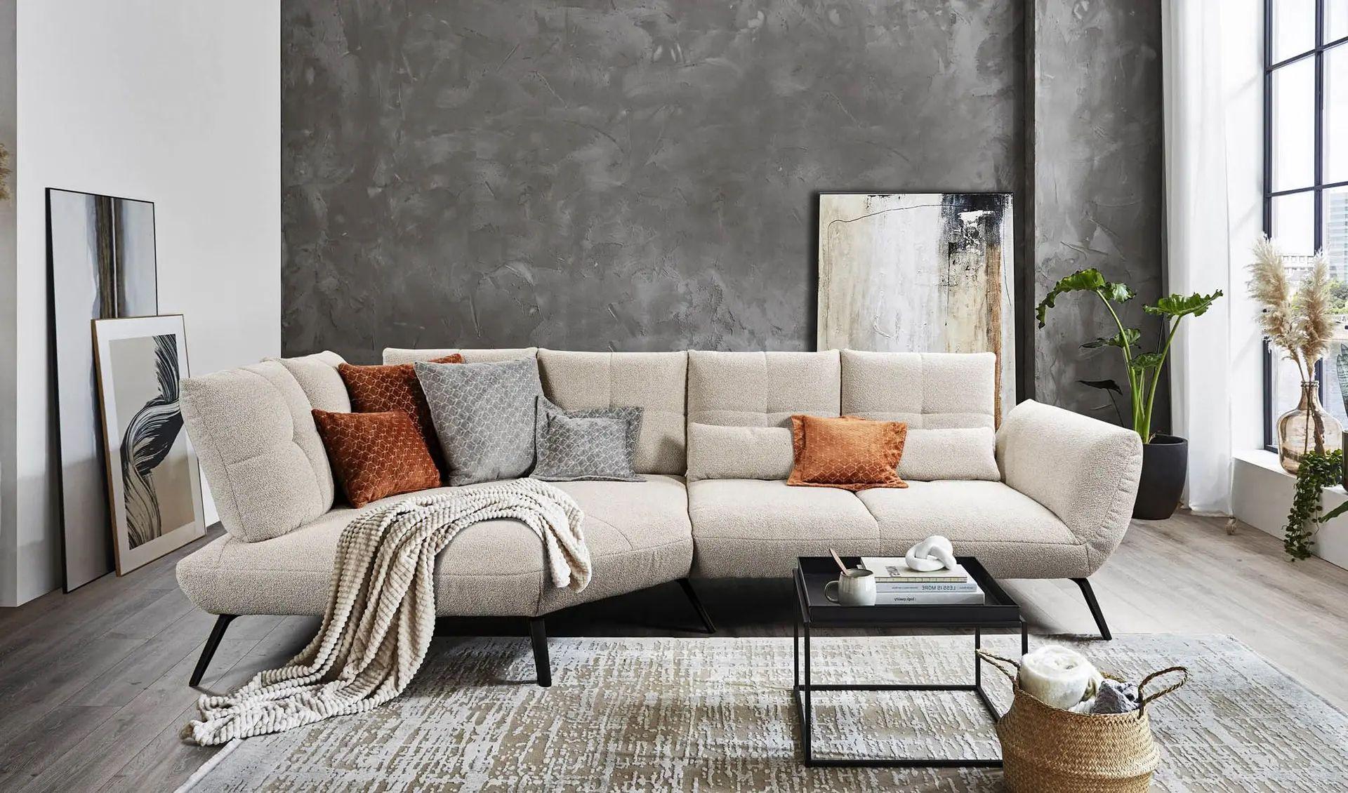Modernes beigefarbenes Ecksofa mit dekorativen Kissen und Decke in einem hellen Wohnzimmer mit grauer Akzentwand.
