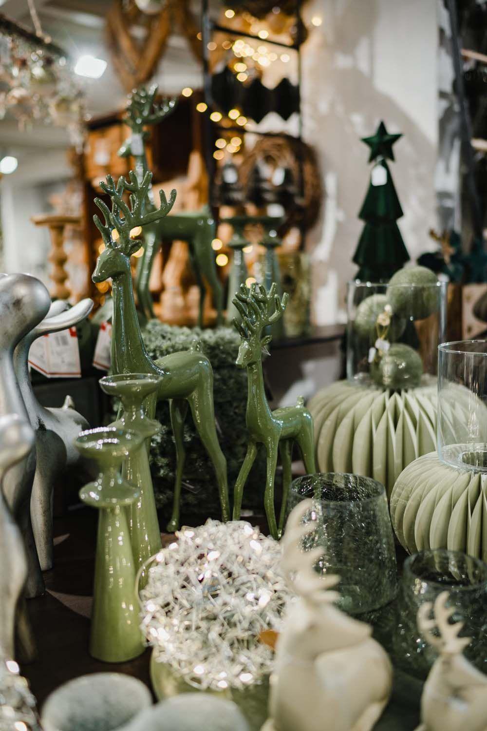 Grüne Weihnachtsdekoration mit Rentierfiguren, Windlichtern und gläsernen Ornamenten.