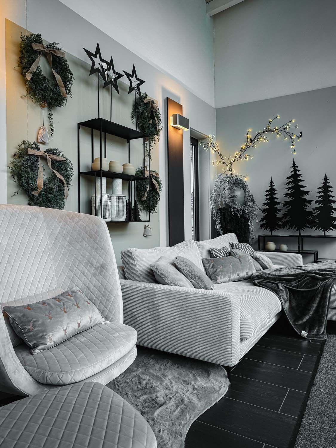 Gemütlicher Wohnbereich in Grau mit weihnachtlichen Kränzen, Stern-Dekoration und warmen Lichtelementen.