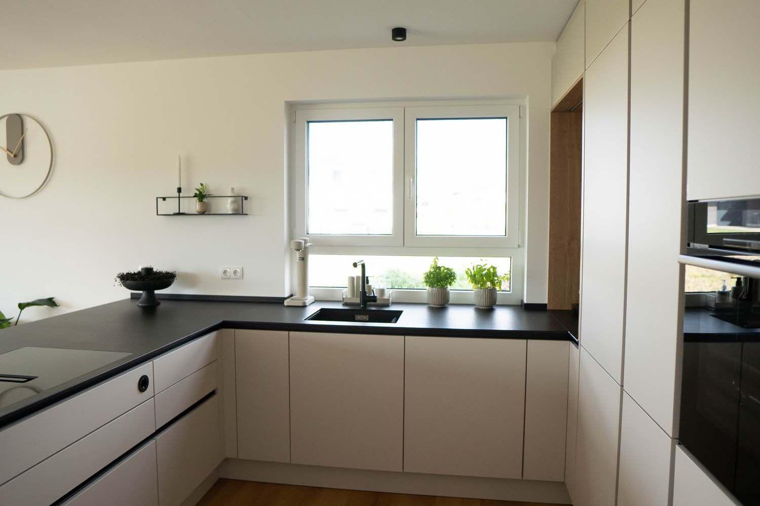 Spülenbereich am Fenster mit schwarzer Arbeitsplatte, hellen Küchenfronten und integrierter Hochschrankwand.