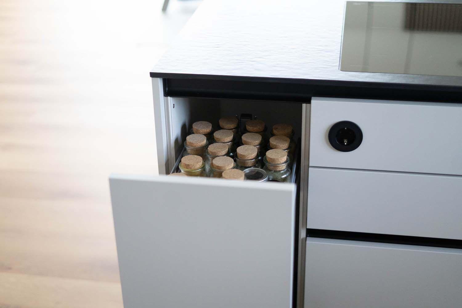 Geöffneter Gewürzauszug mit kleinen Vorratsgläsern in moderner griffloser Küche