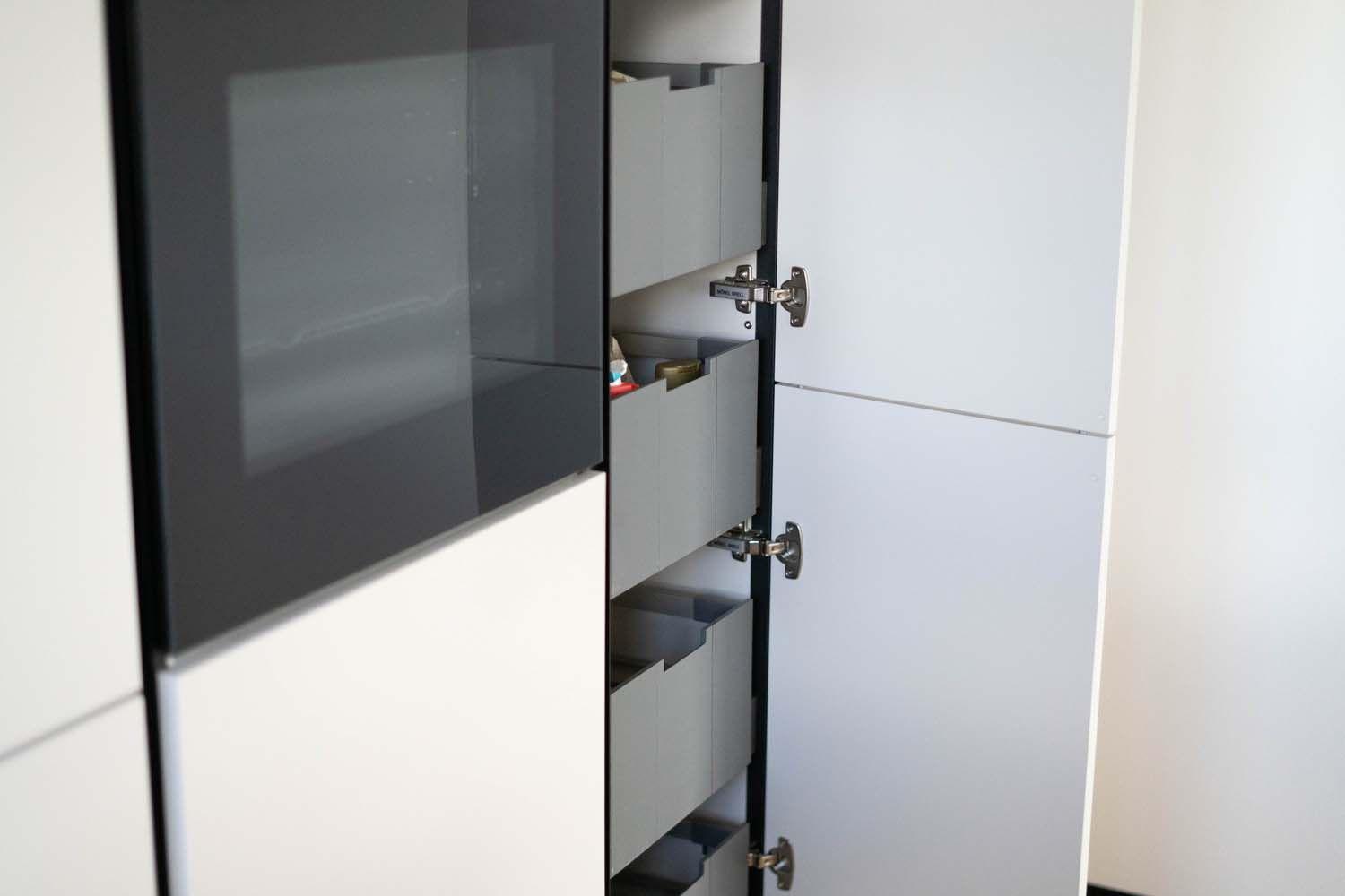 Geöffneter Hochschrank mit Innenauszügen neben dem eingebauten Backofen