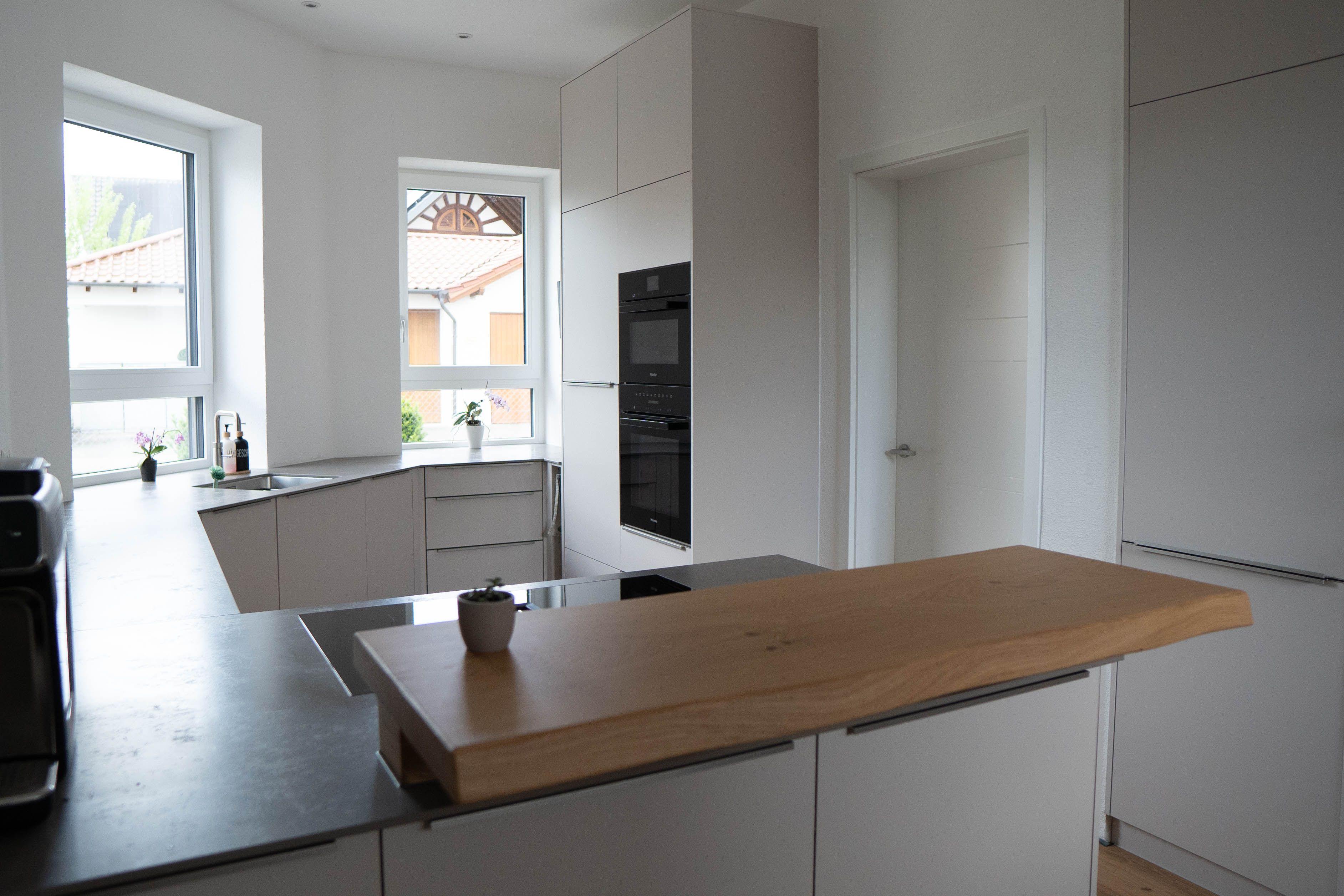 Moderne helle Küche mit aufgesetzter Holztheke, grauer Arbeitsplatte, Spülenbereich am Fenster und Backofen.