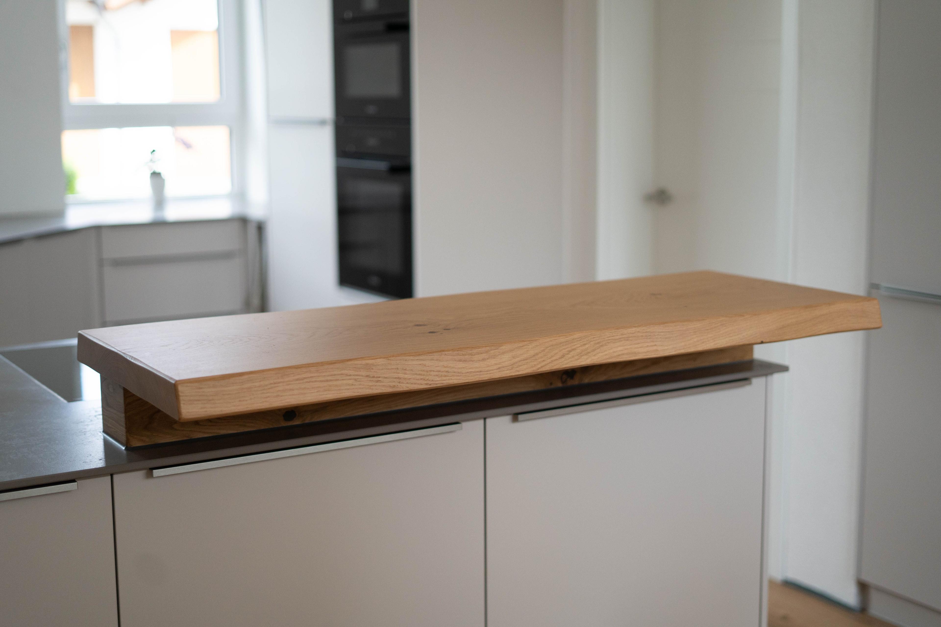 Aufgesetzte Massivholz-Theke auf heller Kücheninsel mit grauer Arbeitsplatte und klaren Fronten.