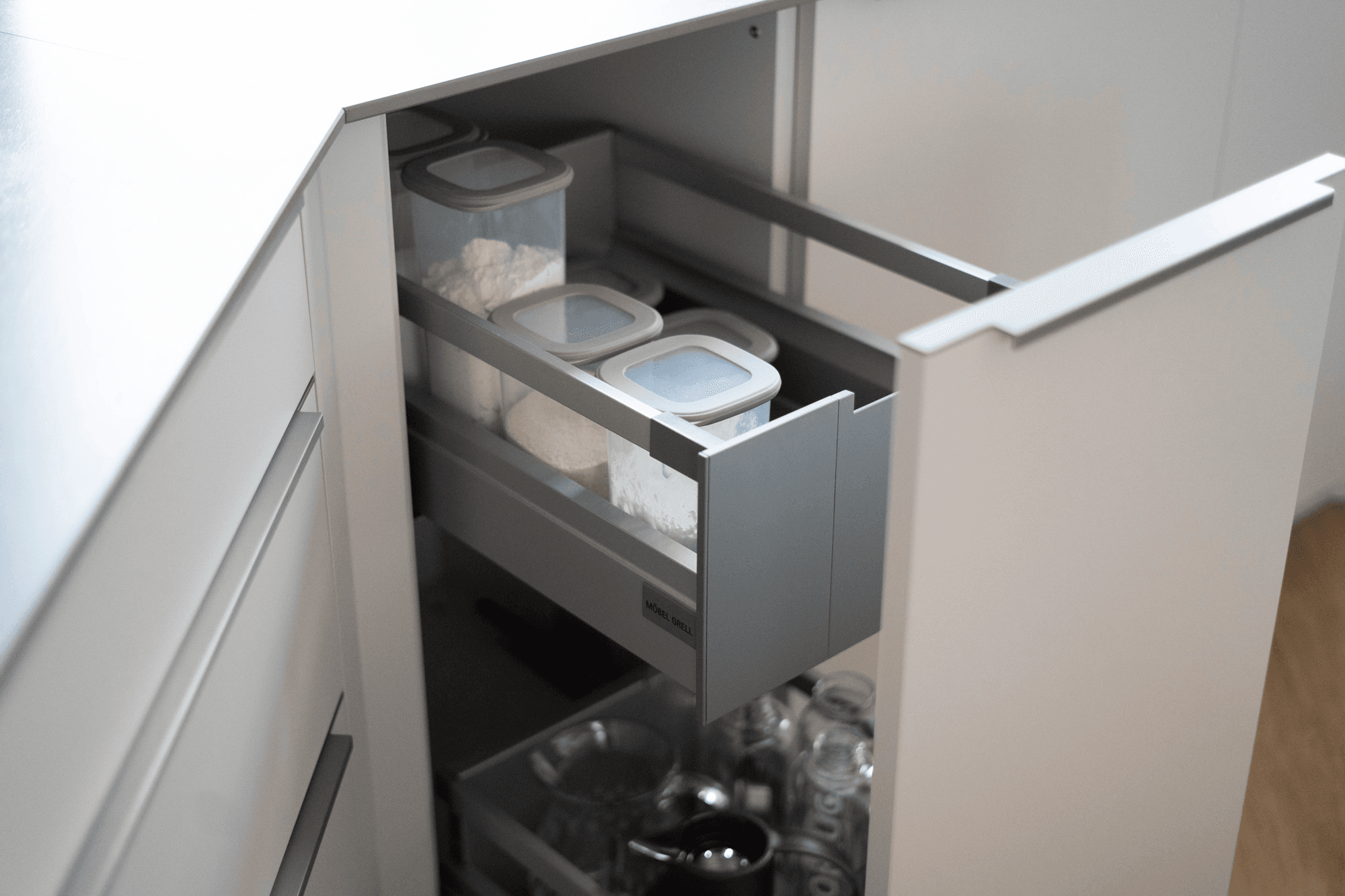 Geöffneter Vorratsauszug mit Aufbewahrungsdosen, Gläsern und Flaschen in heller moderner Küche.