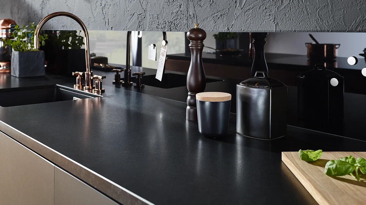 Schwarze Quarzstein-Arbeitsplatte mit Kupfer-Armatur und schwarzer Glas-Rückwand - moderne Arbeitsplatten-Kombinationen.