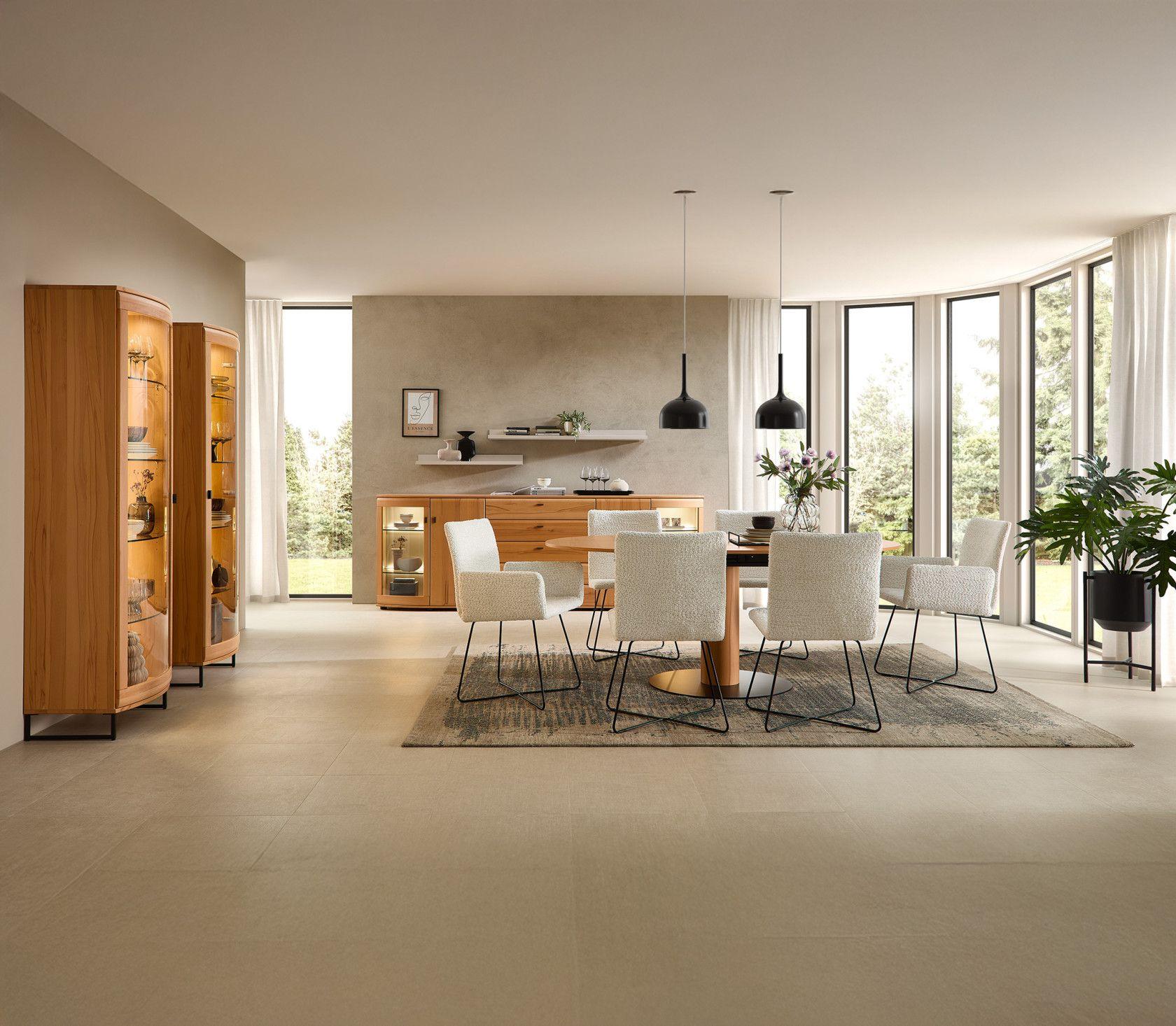 Modern eingerichteter Essbereich mit rundem Holztisch, hellen Stühlen, beleuchteten Vitrinen und Sideboard aus massiver Kernbuche – lichtdurchfluteter Raum mit Panorama-Fenstern.