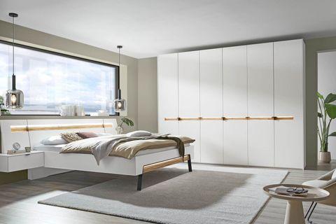 Modernes Schlafzimmer mit weißem Schwebebett, großem weißen Kleiderschrank mit Holzgriffen und Panoramafenster.