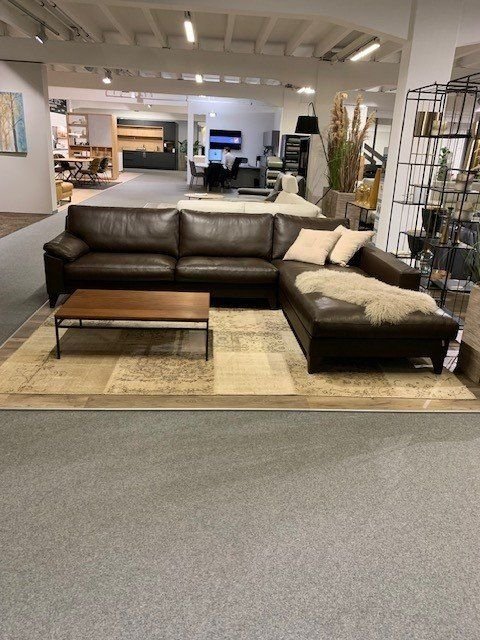 Schwarze Leder-Eckcouch mit Chaiselongue und Holz-Couchtisch in großem Möbelhaus-Showroom.