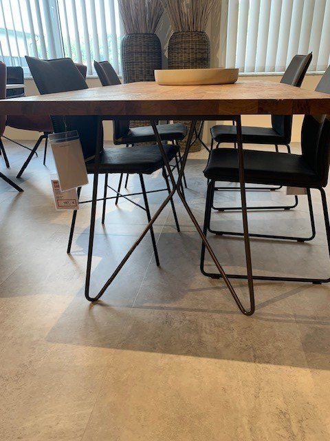 Massivholz-Esstisch mit schwarzen Metallstühlen in lichtdurchflutetem Showroom mit Lamellenvorhängen und dekorativen Weidenkörben.